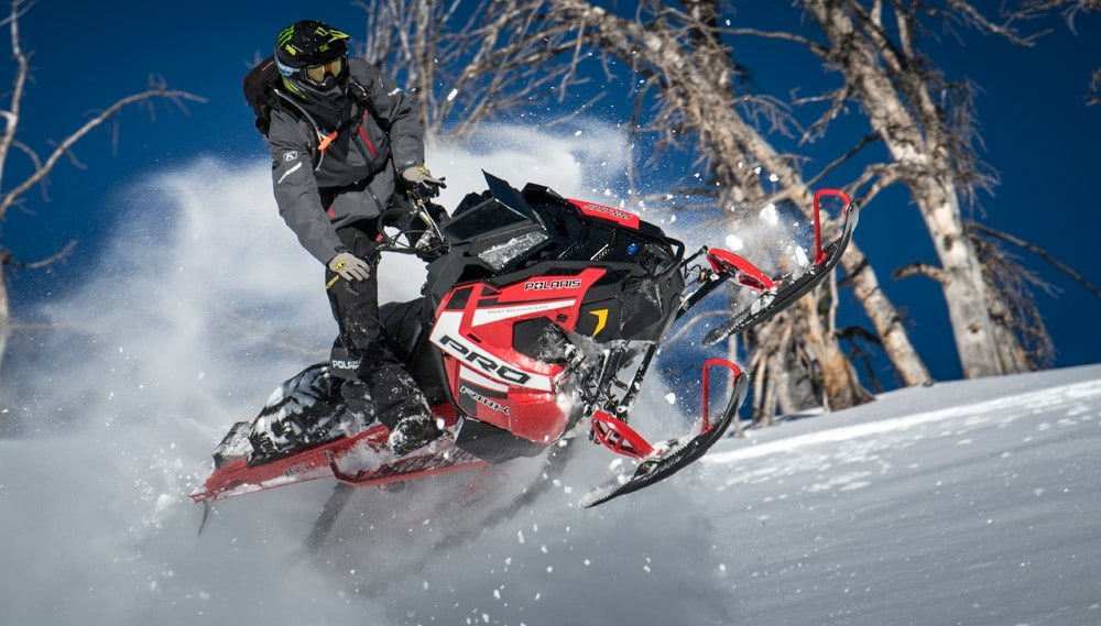 Image of a man driving a red Polaris snowmobile in the mountains in winter